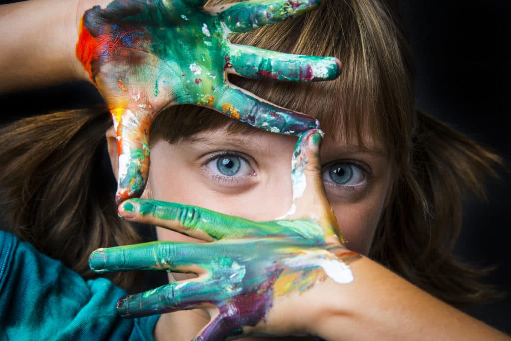 Mädchen rahmt, mit ihren Fingern voller Farbe, ihr Auge ein.