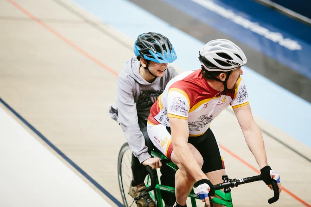 Ein Kind fährt auf einem Tandem mit einem unserer Radrennprofis.