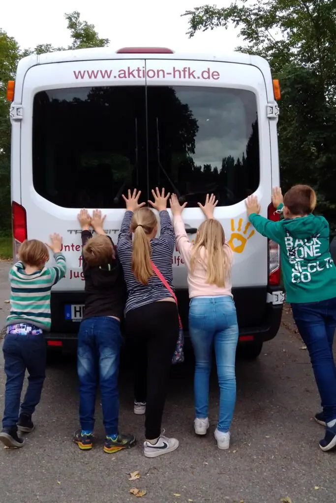 Eine Guppe Kinder schieben einen Bus von hinten an.