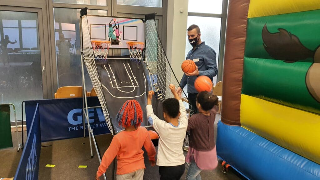 Kinder spielen ein Basketball-Spiel unter Aufsicht eines Mitarbeiters.