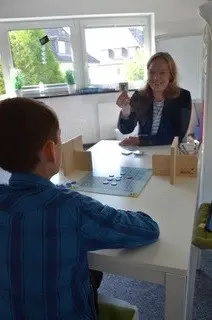 Ein Kind bekommt Förderunterricht von einer Frau hinter einer Glasscheibe.